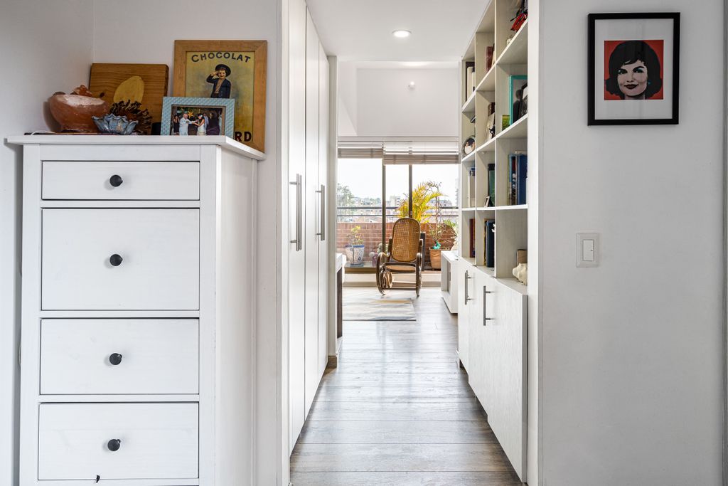 Un pasillo moderno con espacio de almacenamiento que conduce a una habitación luminosa con una mecedora, en Bogotá, Colombia.